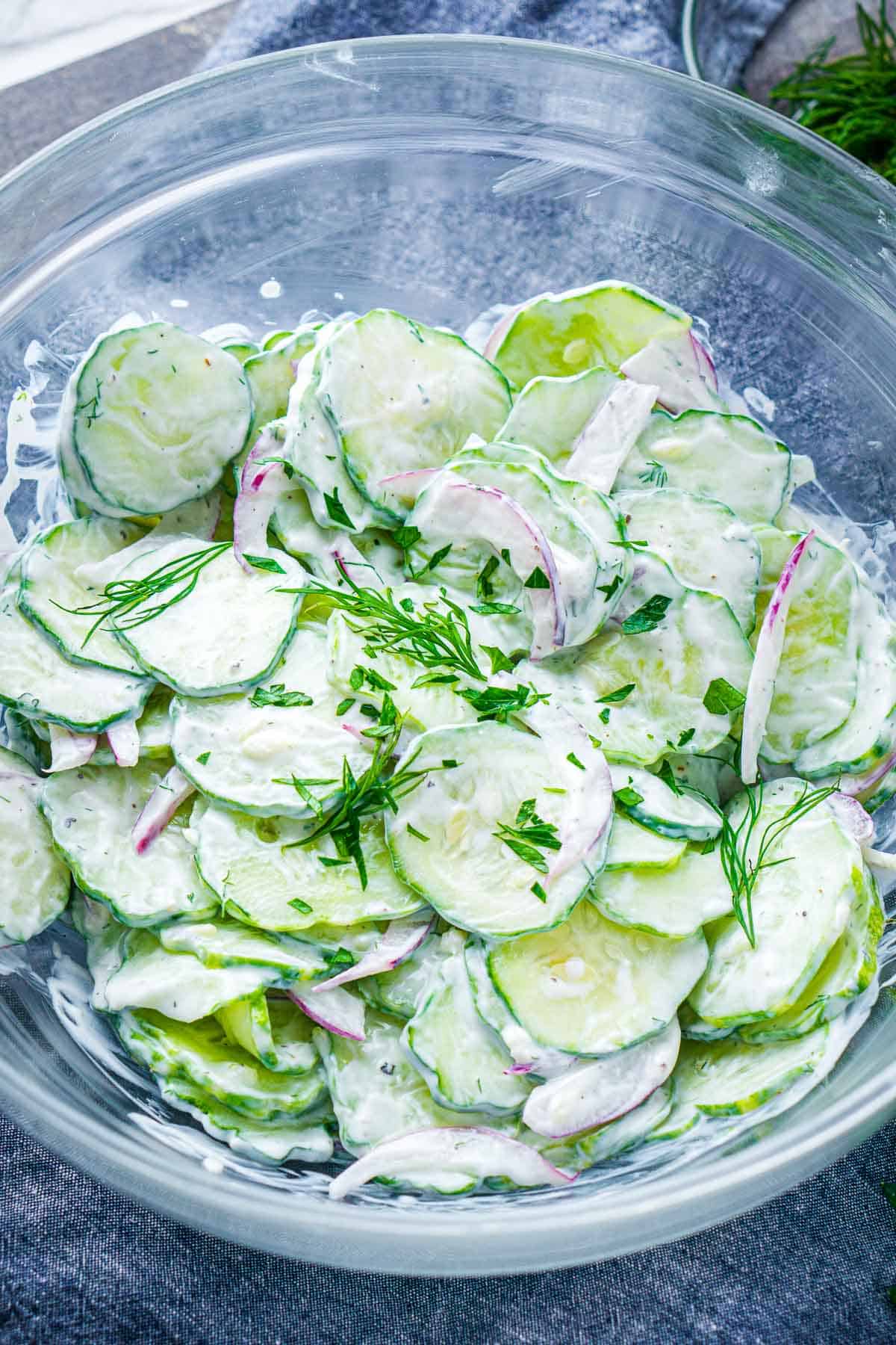 creamy cucumber salad with serving spoon in glass bowl on blue linen