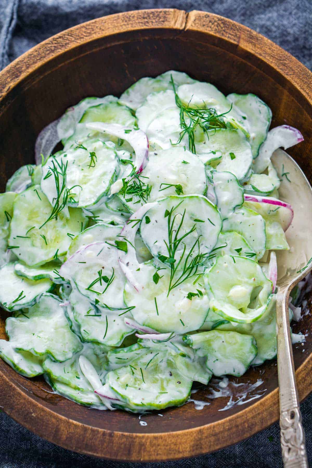 creamy cucumber salad with serving spoon in wood bowl on blue linen