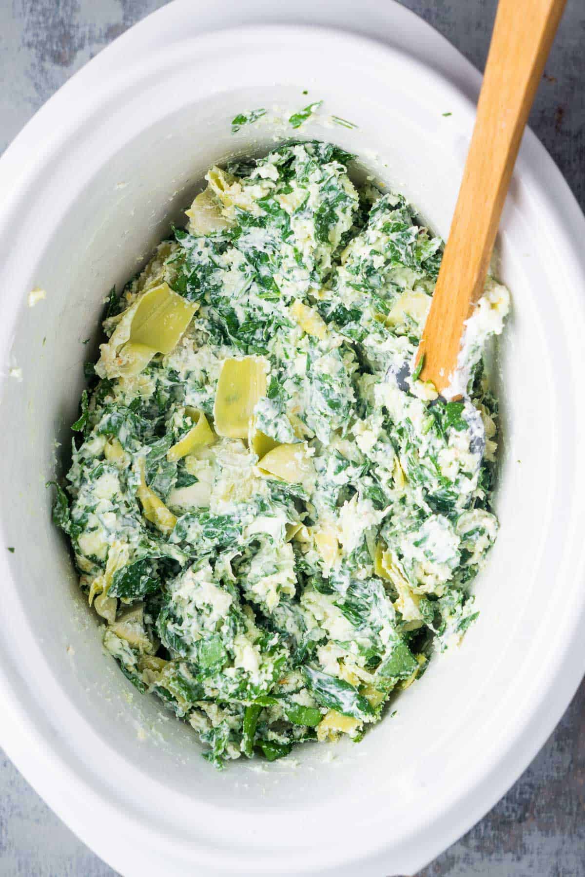 Spinach artichoke dip ingredients are stirred in slow cooker