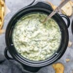 Spinach artichoke dip in a slow cooker with a spoon
