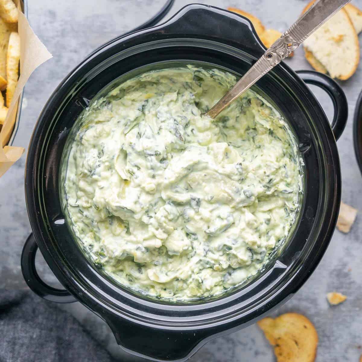 Spinach artichoke dip in Crockpot with a spoon