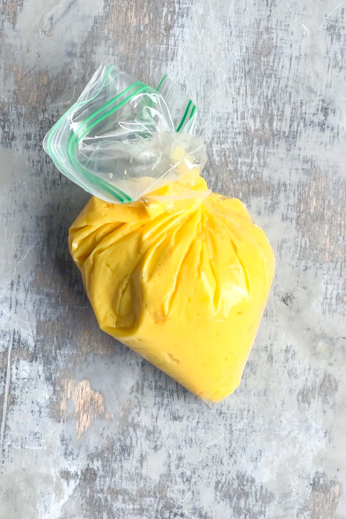 A clear plastic zip-top bag filled with yellow deviled eggs filling, placed on a gray textured surface.