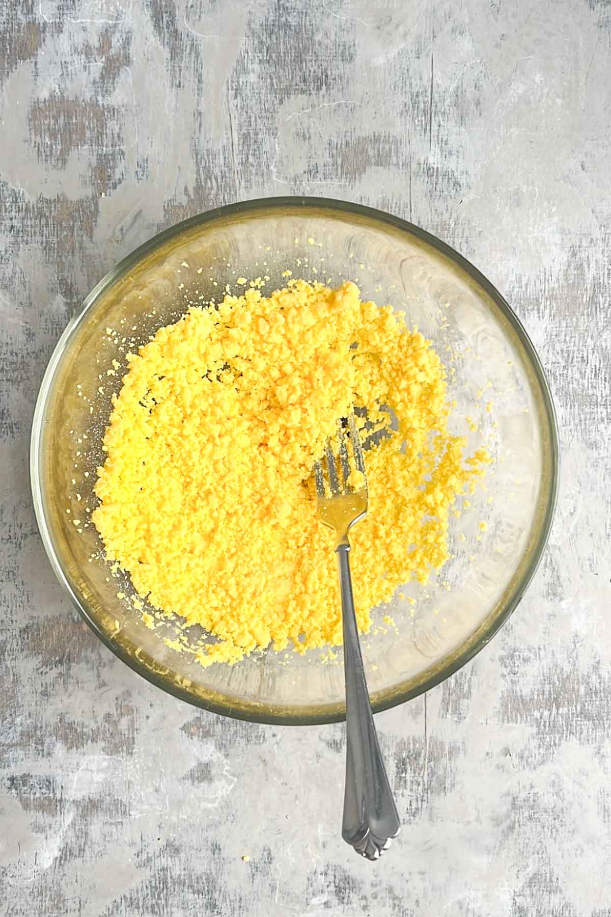 A glass bowl containing finely crumbled hard-boiled egg yolks with a fork resting inside.