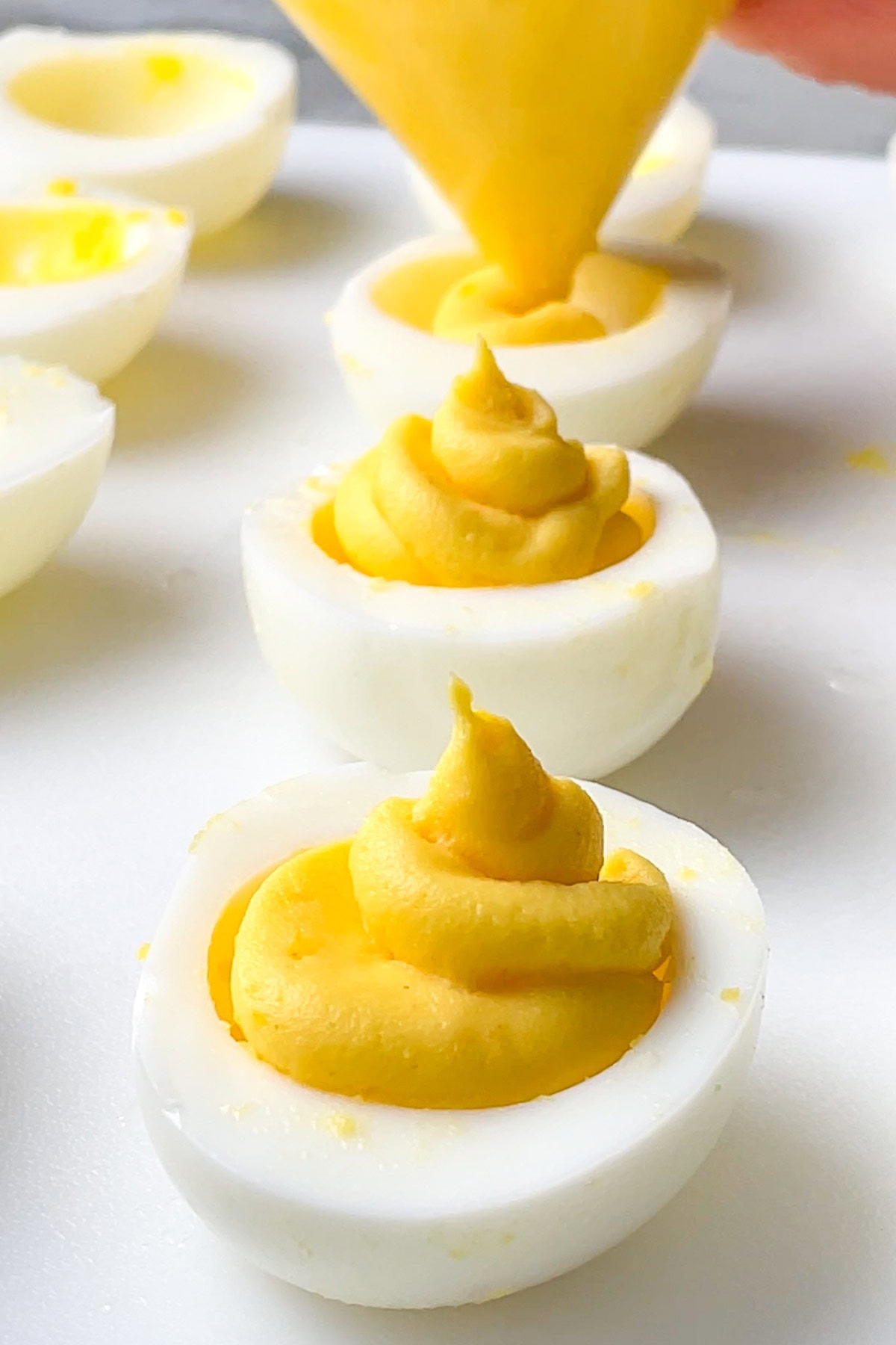 A close-up of deviled eggs being filled with a creamy yellow filling using a piping bag on a white surface.