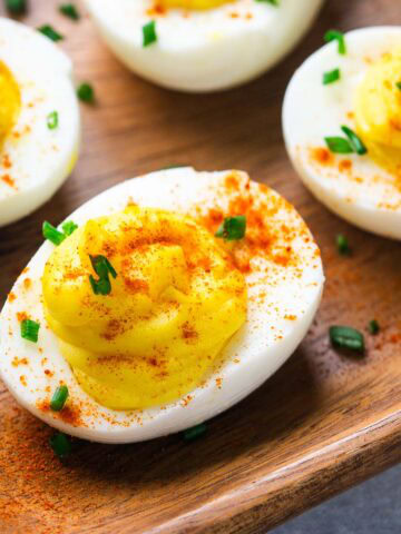 Several deviled eggs on a wooden tray, topped with paprika and chopped chives, make a classic appetizer everyone will love.
