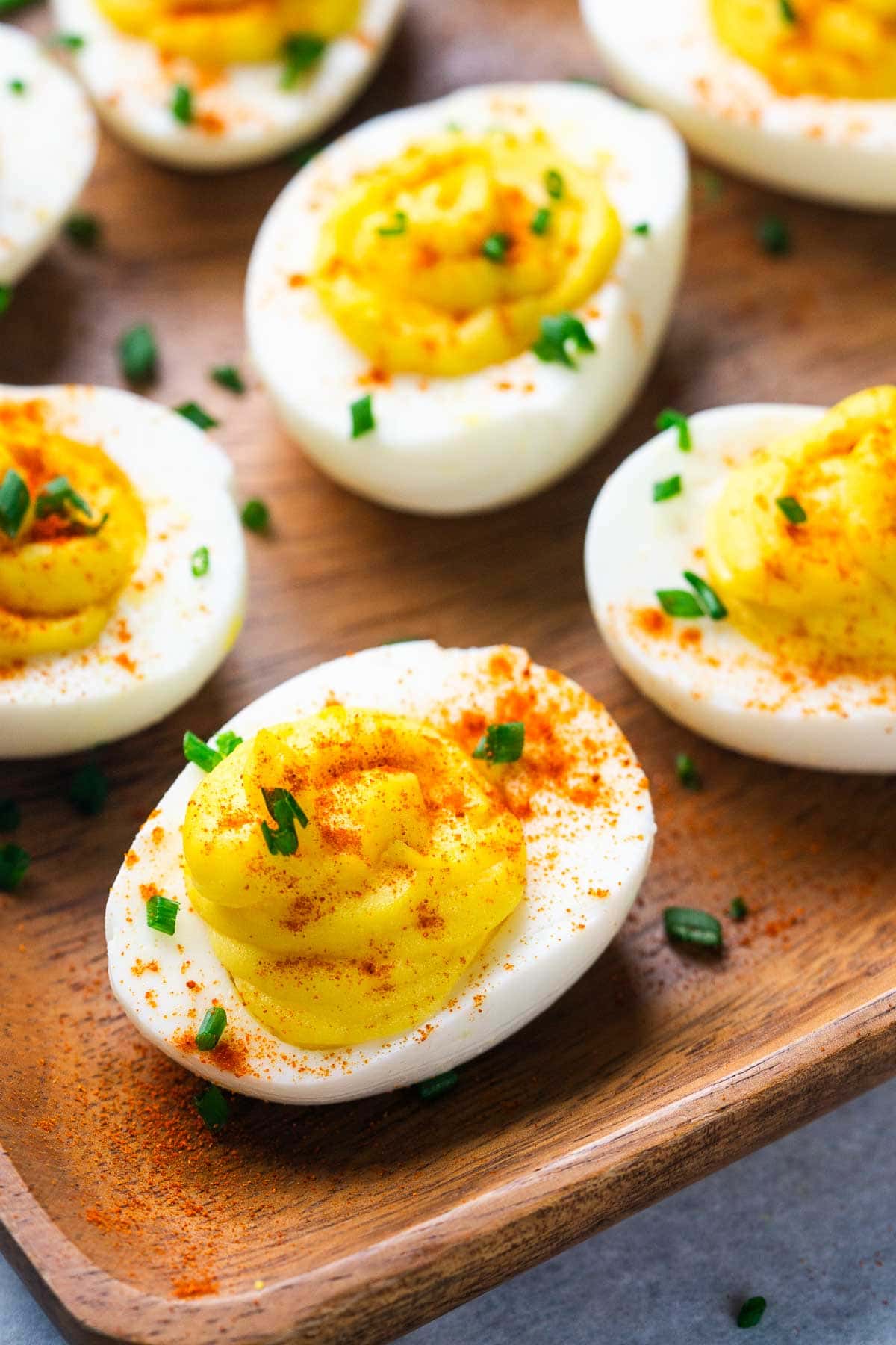 Several deviled eggs on a wooden tray, topped with paprika and chopped chives, make a classic appetizer everyone will love.