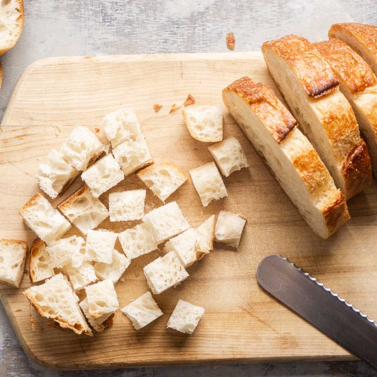 sliced bread and bread cubes on wood cutting board with serrated bread knife