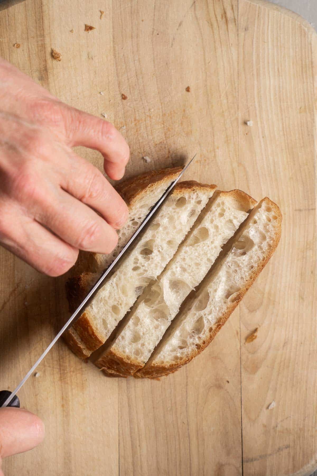 person's hand slicing bread into strips for bread cubes