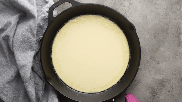 Dutch baby batter in iron skillet next to gray linen on gray surface