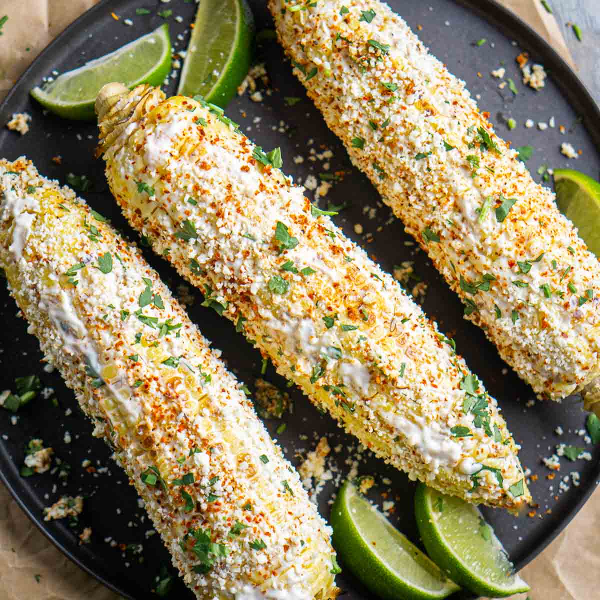 elote street corn on black plate garnished with lime wedges