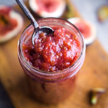 fig jam in glass jar on cutting board with scattered fresh fig pieces