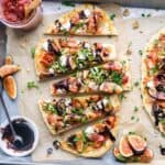 fig prosciutto flatbread pizza slices on parchment paper next to toppings