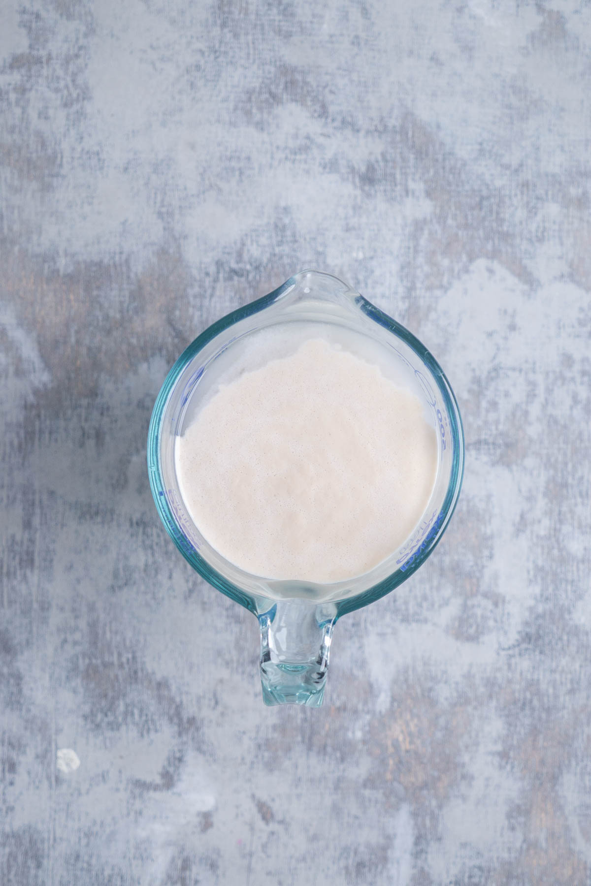 Overhead shot of bloomed yeast in water in glass measuring cup.