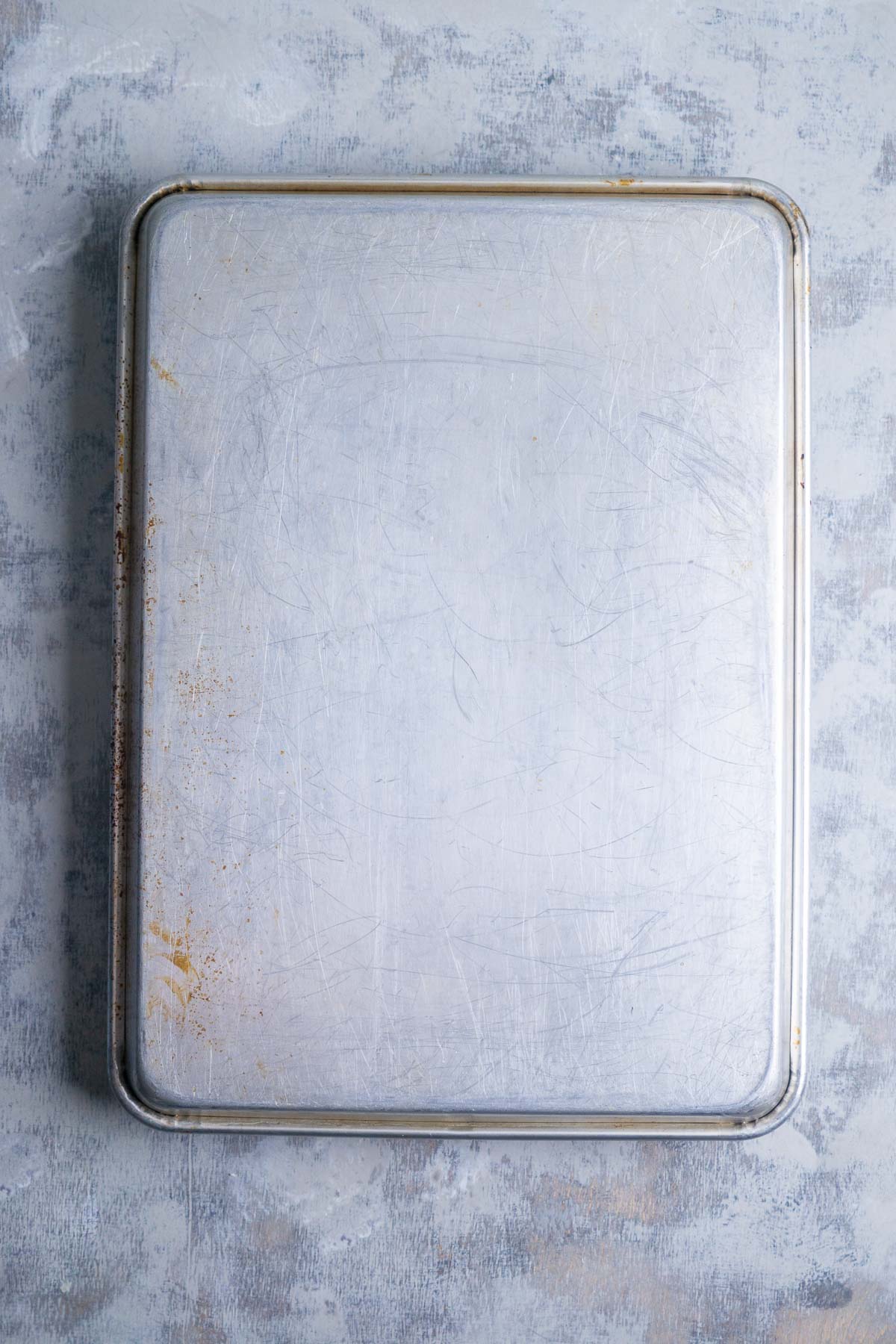 A rectangular metal baking sheet is inverted over a pan of focaccia dough.