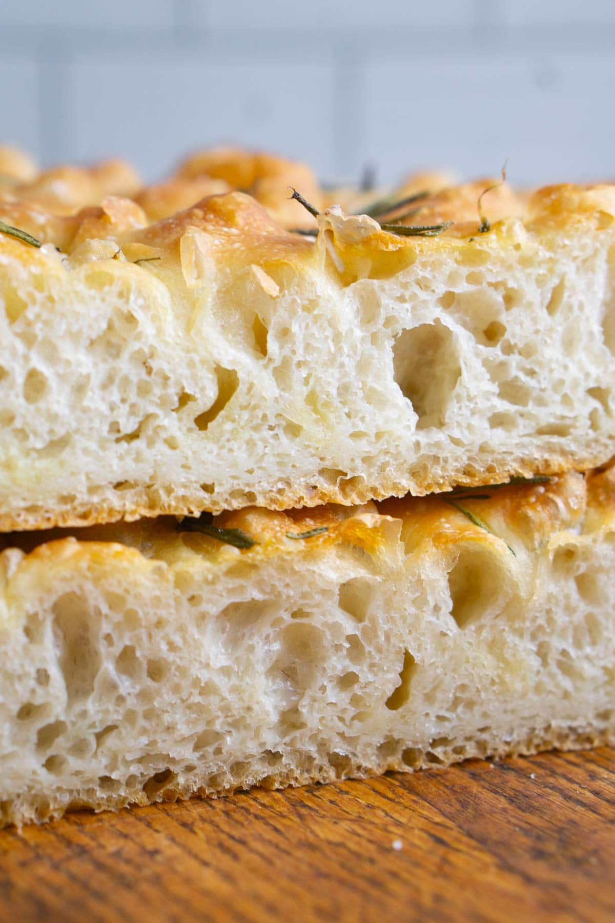 Close-up of two slices of airy, golden-brown focaccia bread stacked on a wooden surface, highlighting the open crumb structure typical of authentic focaccia bread.