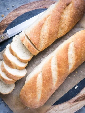 partially sliced French bread on cutting board next to bread knife