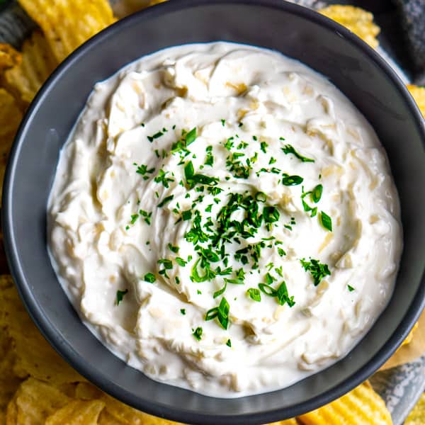 French onion dip in black bowl over platter of potato chips