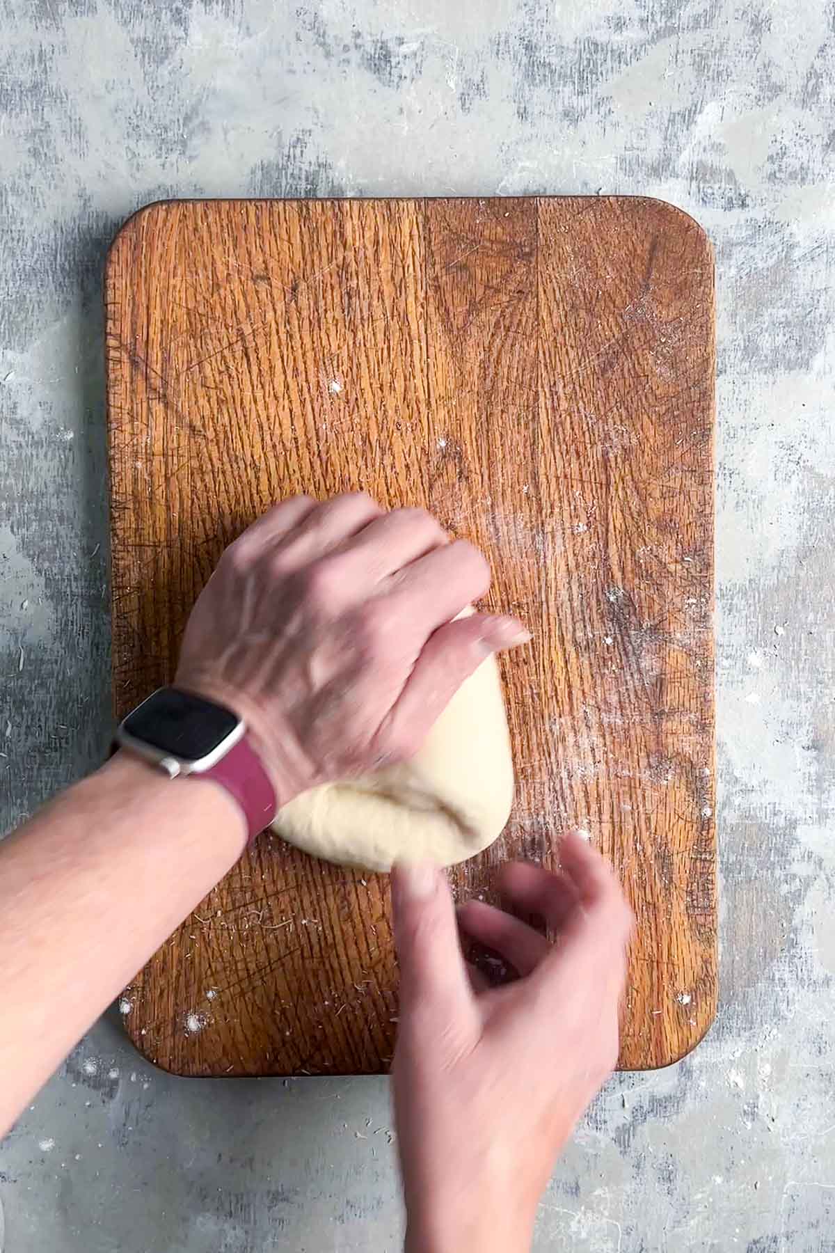 Two hands kneading dough on a wooden cutting board for naan bread.