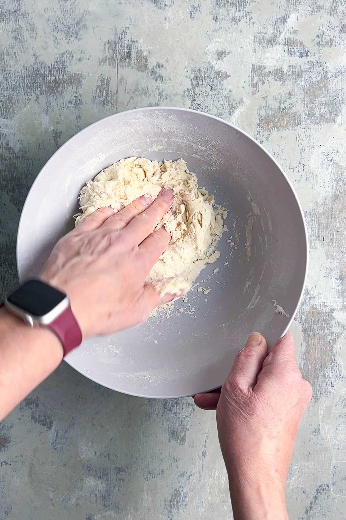 A person uses their hand to mix dough for naan bread in a large gray bowl.