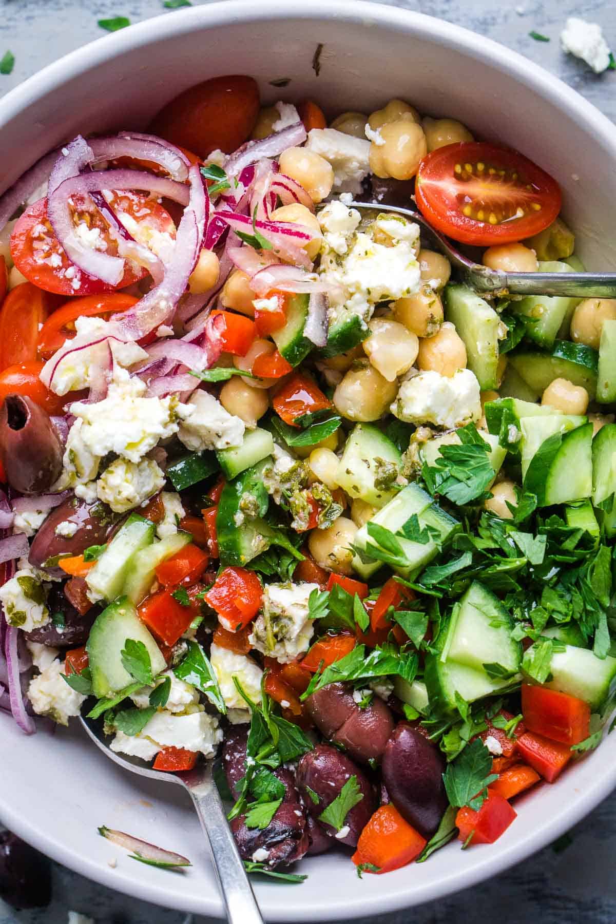 Greek chickpea salad in white bowl being tossed with two spoons
