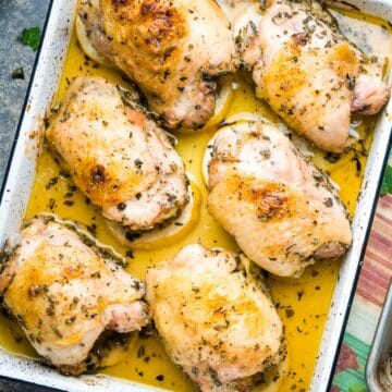 Greek chicken thighs on white baking sheet