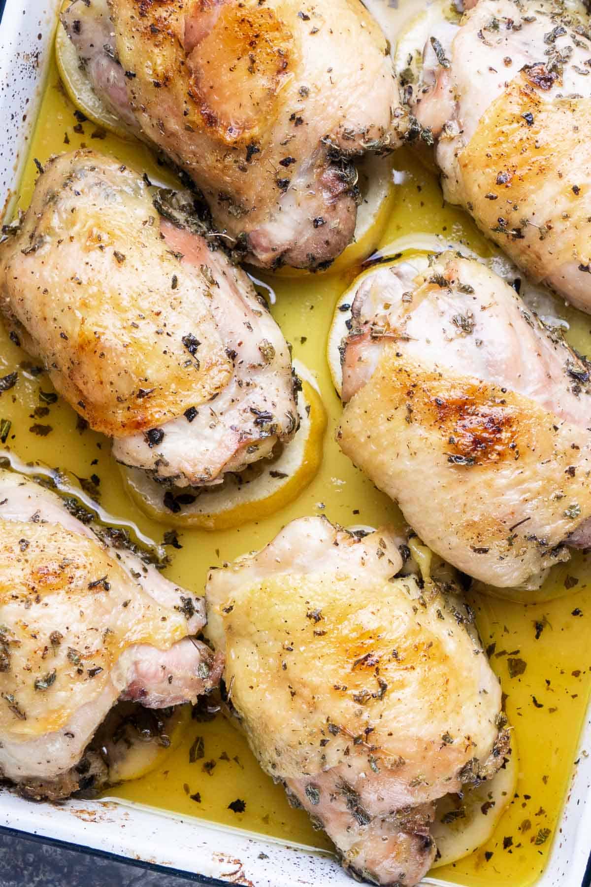 baked chicken thigh pieces rest on lemon beds on white baking sheet