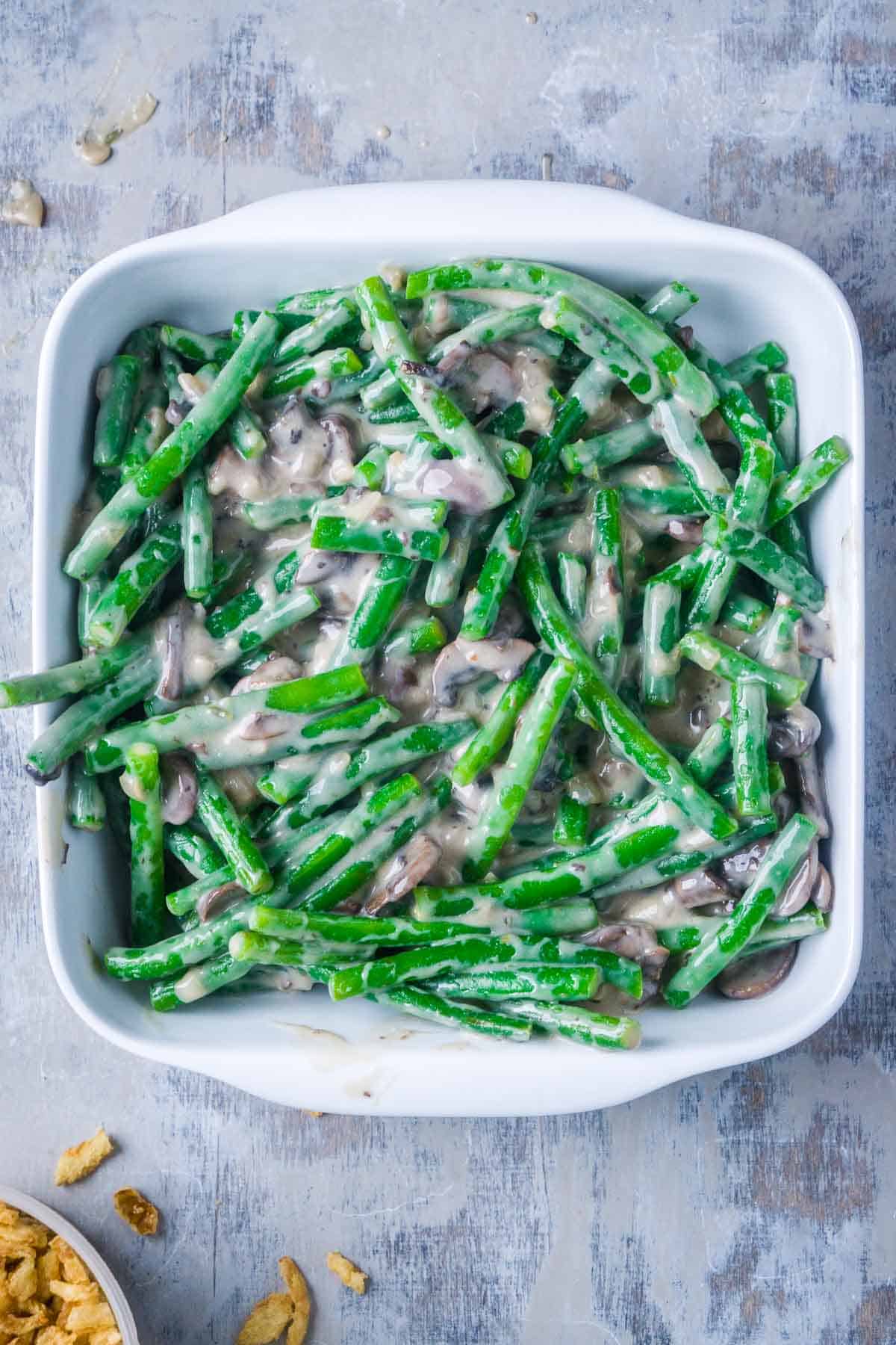 blanched green beans coated with mushroom soup in white baking dish