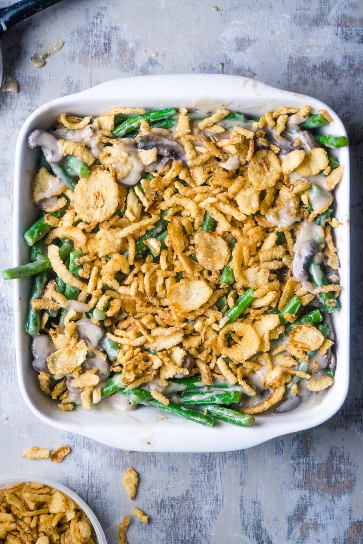 unbaked green bean casserole with crispy French onion topping in white baking dish