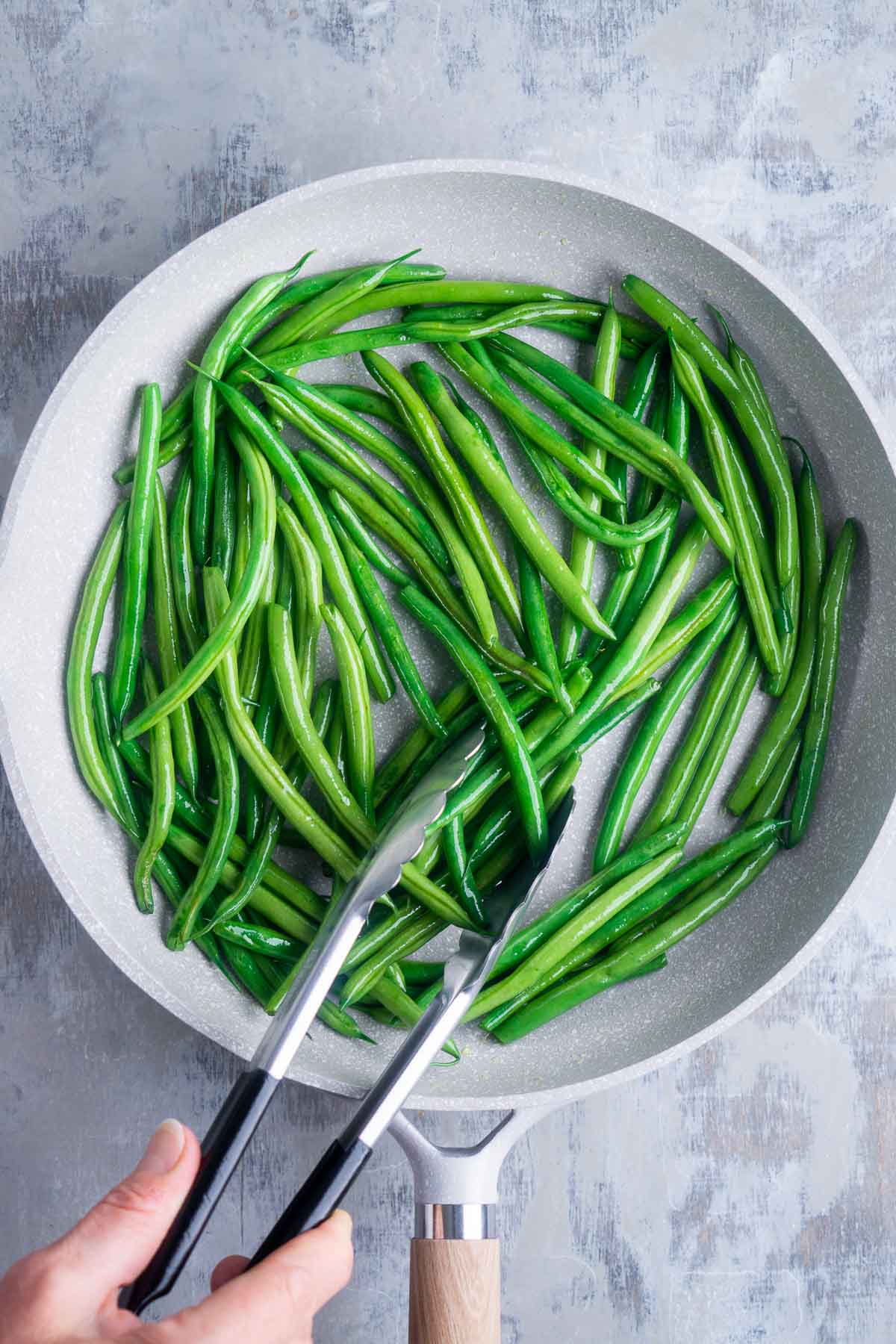 green beans sauteing in skillet are tossed with tongs