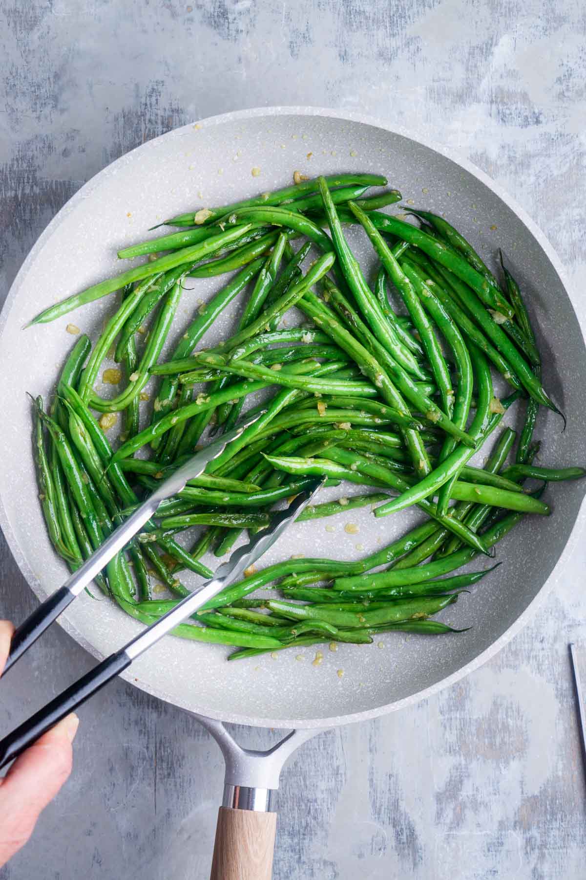 green beans sauteing in skillet are tossed with tongs