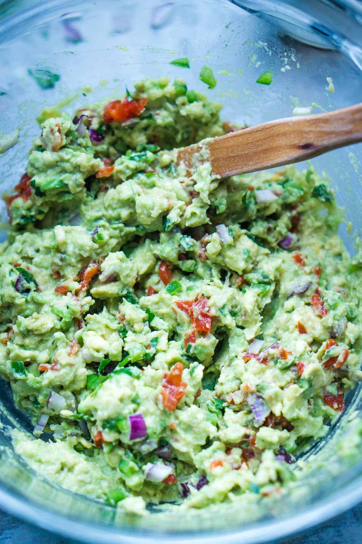 wooden utensil stirs guacamole in glass mixing bowl