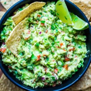 guacamole and lime wedges in black bowl next to tortilla chips