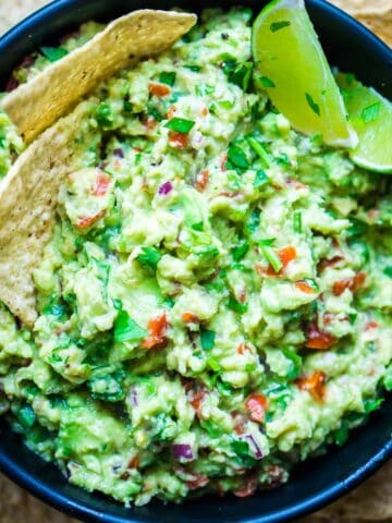 guacamole and lime wedges in black bowl next to tortilla chips