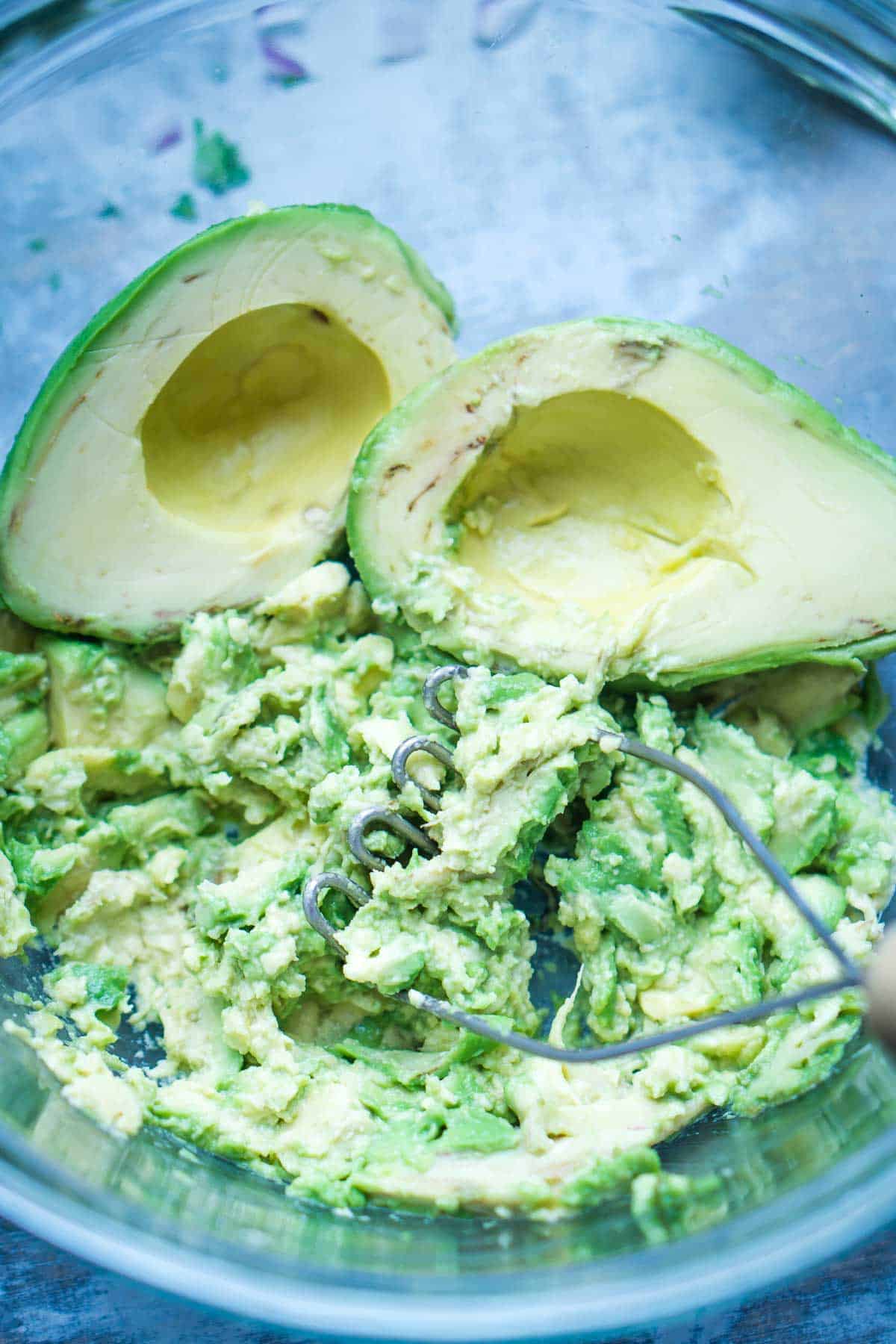 vegetable masher is mashing avocado in glass mixing bowl