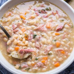 Ham and beans in white bowl with spoon