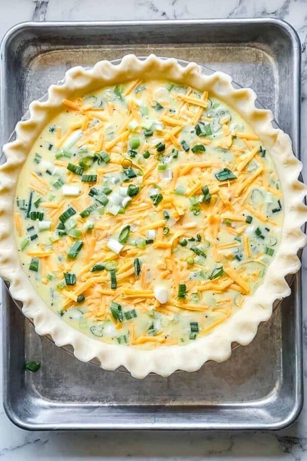 Unbaked ham and cheese quiche in glass pie plate on baking sheet.