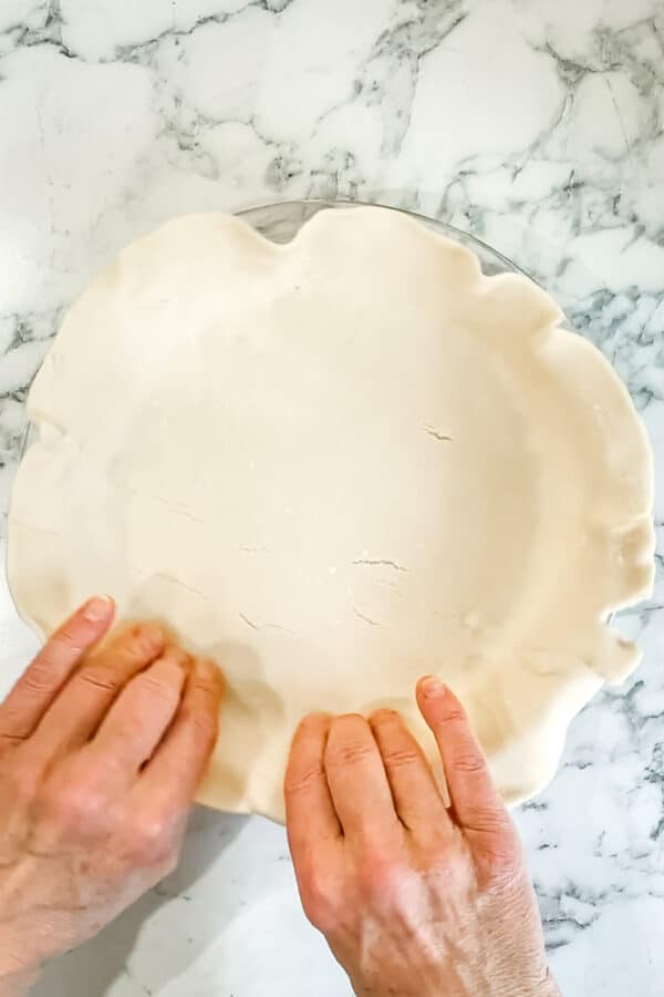 Person's hands pressing pie crust into glass pie plate.