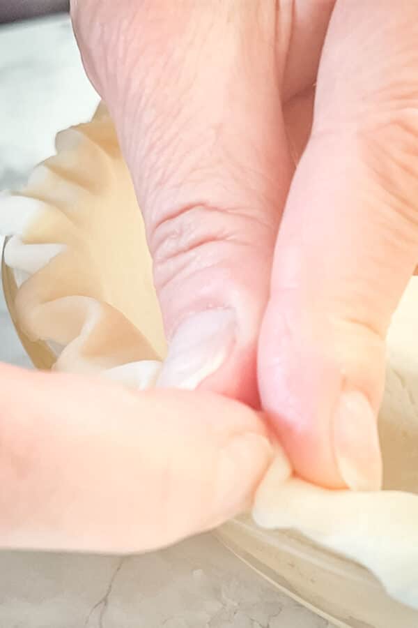 Persons hands crimping pie crust edges.