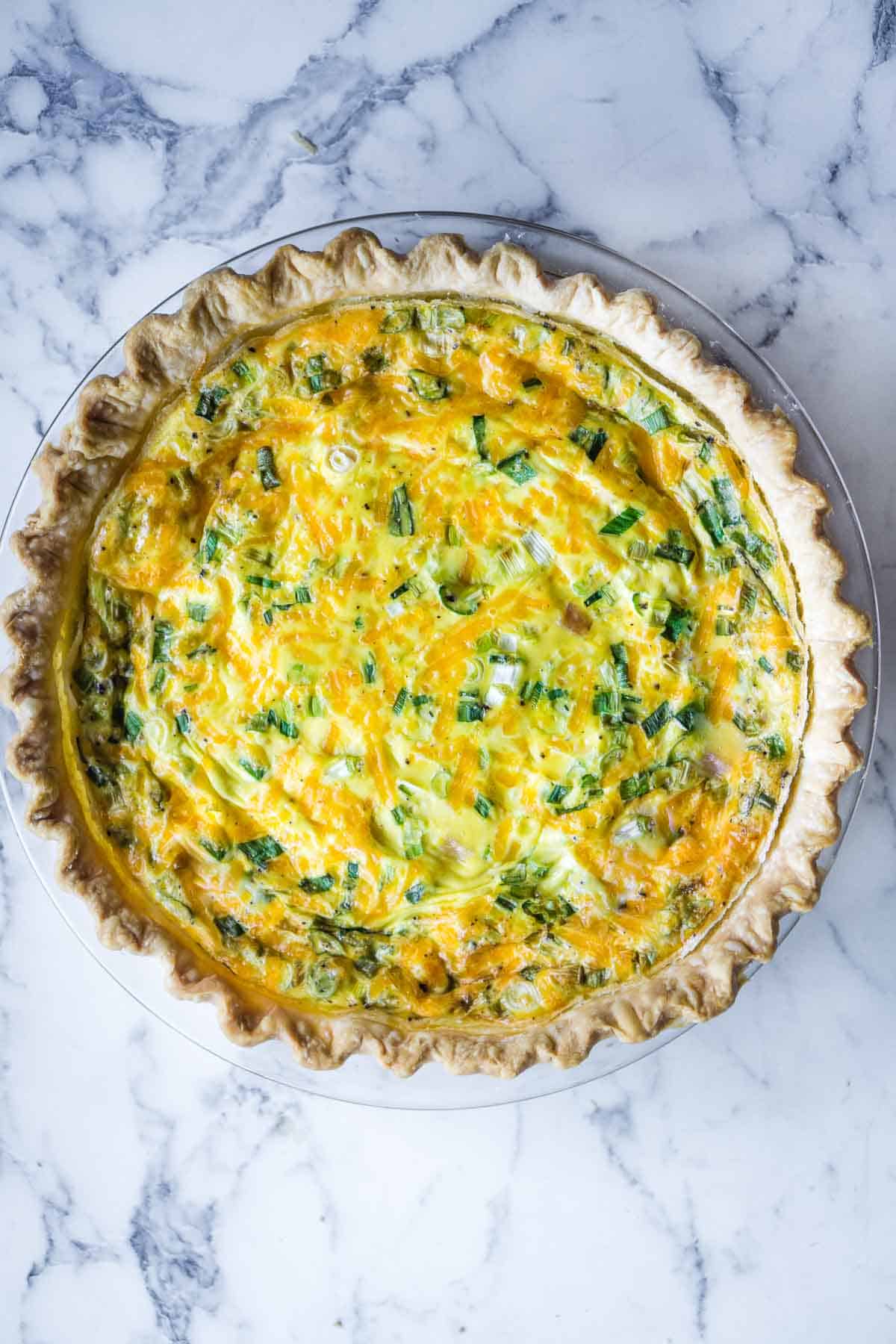 Baked ham and cheese quiche with golden pie crust in glass pie plate.