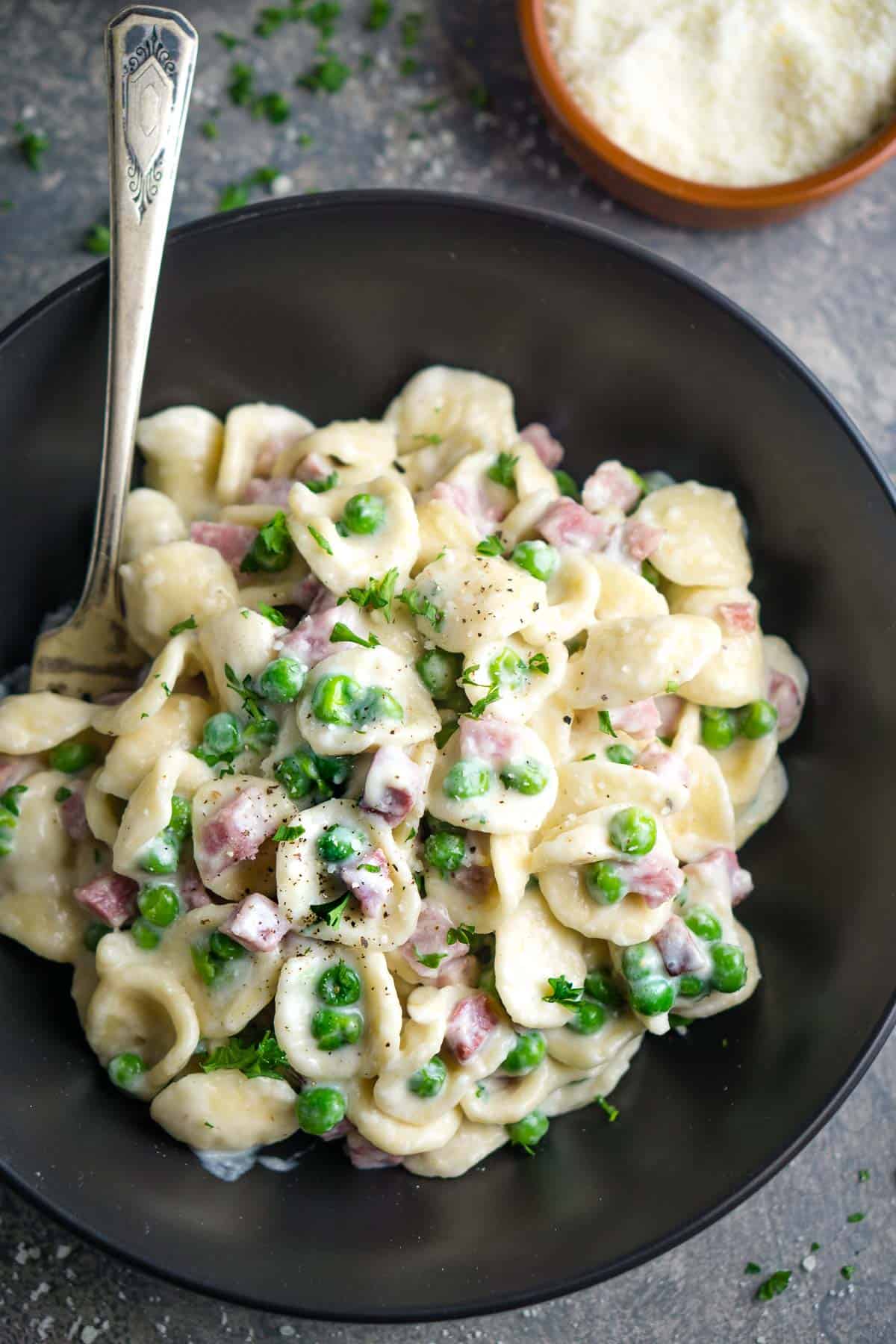 creamy ham and pea pasta in black bowl with fork
