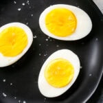 Three hard boiled eggs cut in half on a black plate, their bright yellow yolks exposed and sprinkled with coarse salt.
