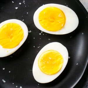 Three hard boiled eggs cut in half on a black plate, their bright yellow yolks exposed and sprinkled with coarse salt.