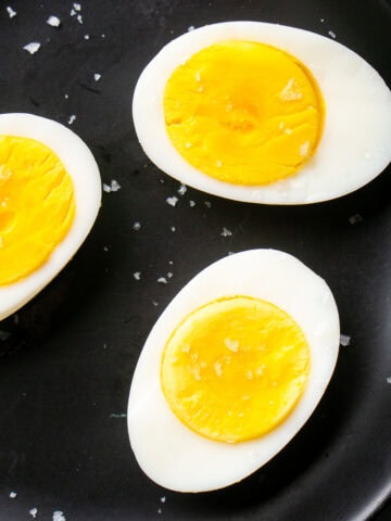 Three hard boiled eggs cut in half on a black plate, their bright yellow yolks exposed and sprinkled with coarse salt.