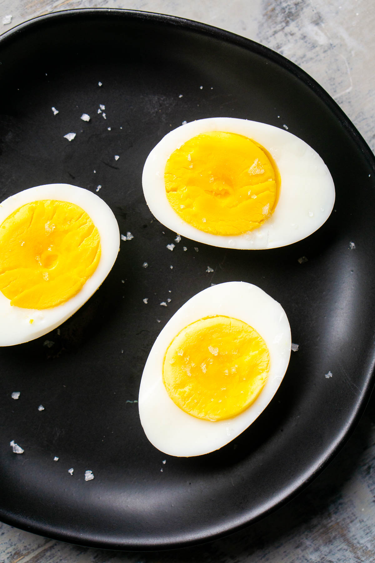 Three hard boiled eggs cut in half on a black plate, their bright yellow yolks exposed and sprinkled with coarse salt.