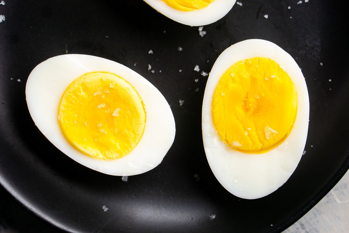 Two hard boiled eggs cut in half on a black plate, their bright yellow yolks exposed and sprinkled with coarse salt.