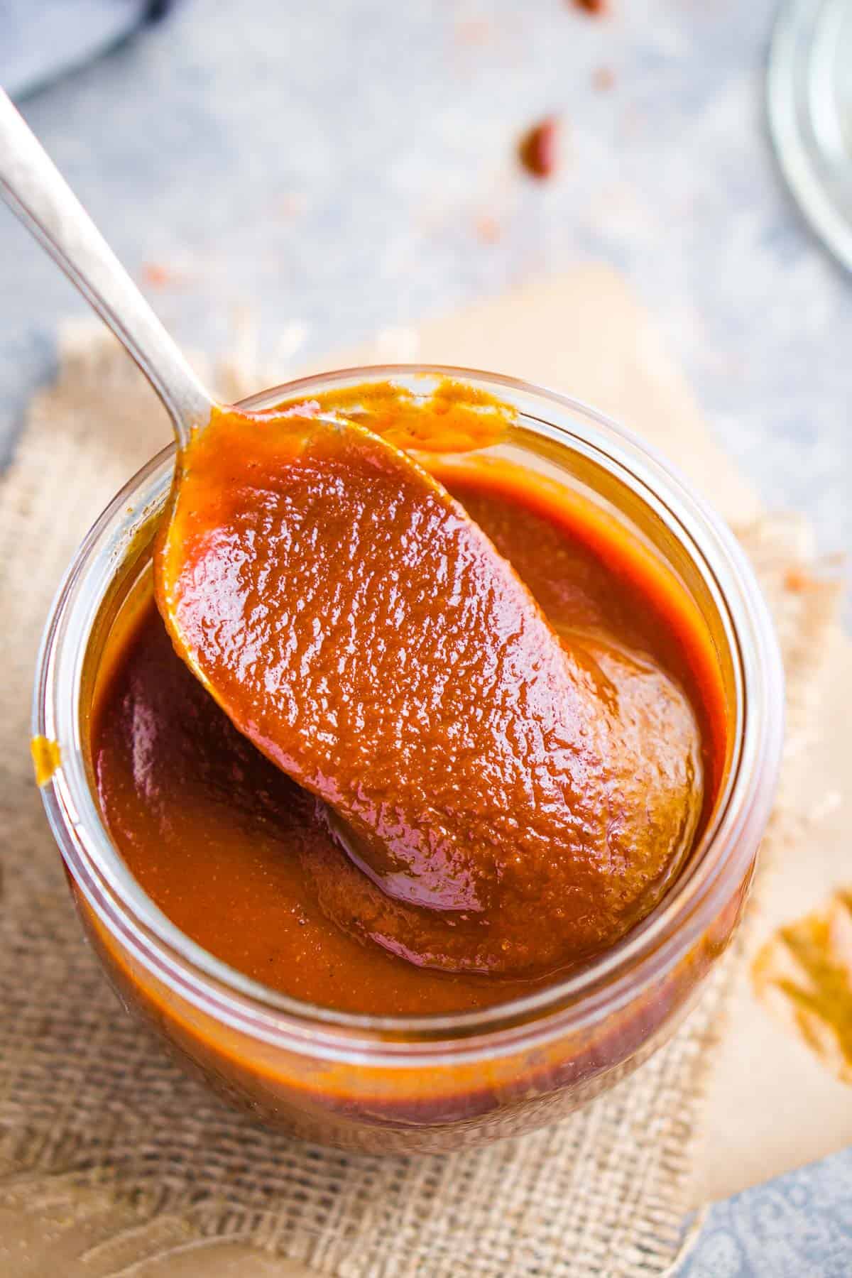 barbecue sauce in glass jar being scooped up with a spoon
