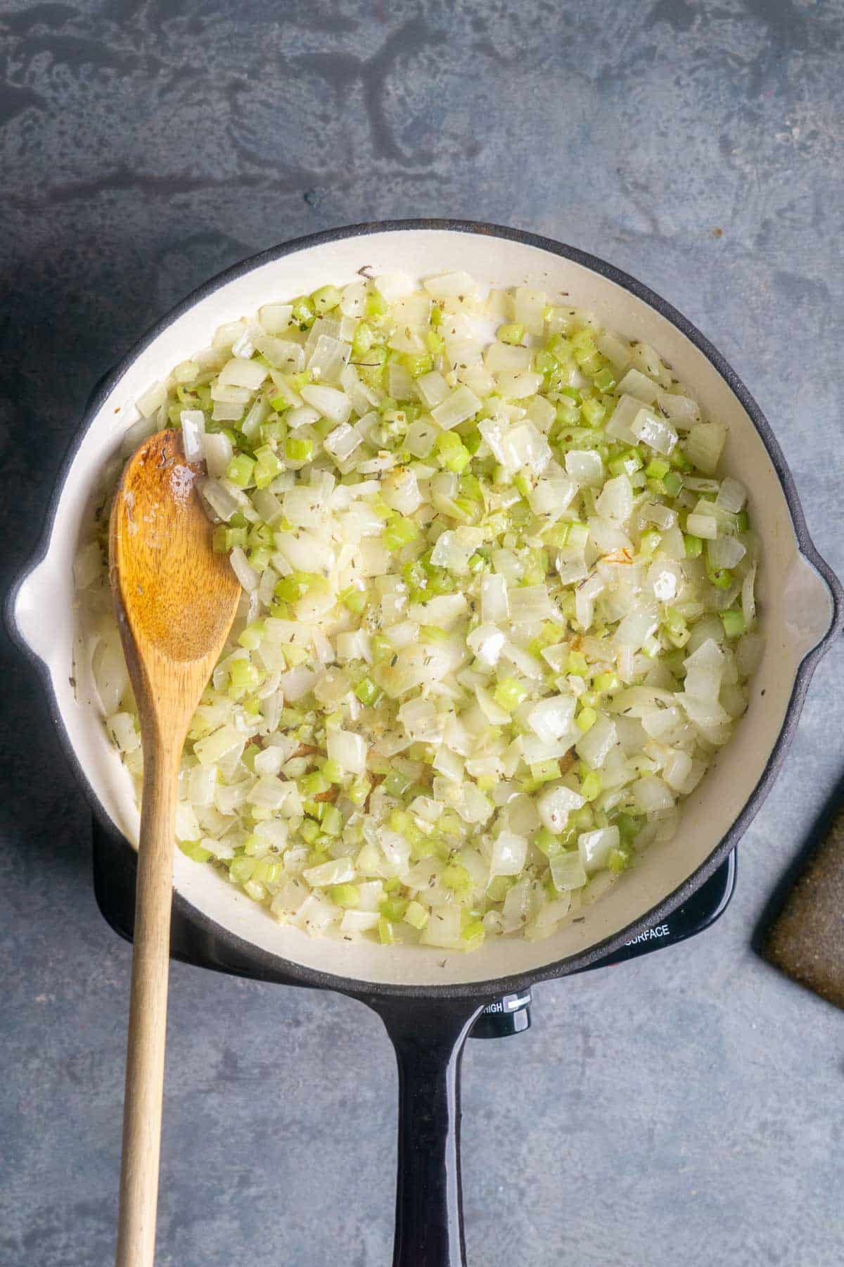 wooden spoon stirs celery and onions sauteing in iron skillet