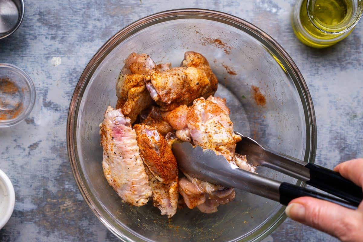 Chicken wings are tossed with seasonings in a mixing bowl