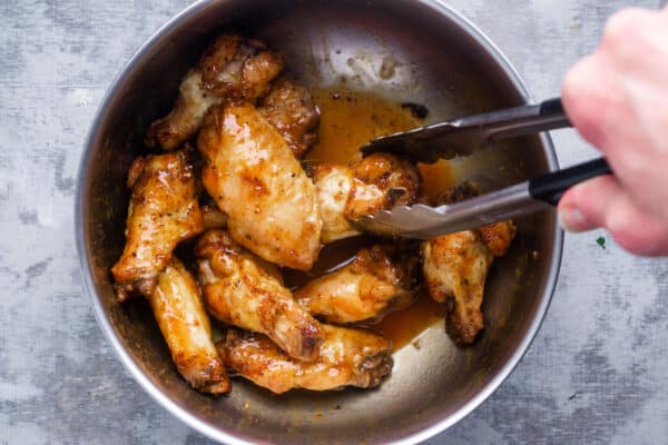 cooked chicken wings are tossed in honey hot sauce in a mixing bowl