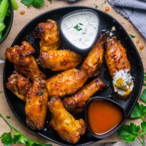 juicy cooked honey hot wings arranged on a black plate with ramekin of ranch dressing and honey hot sauce